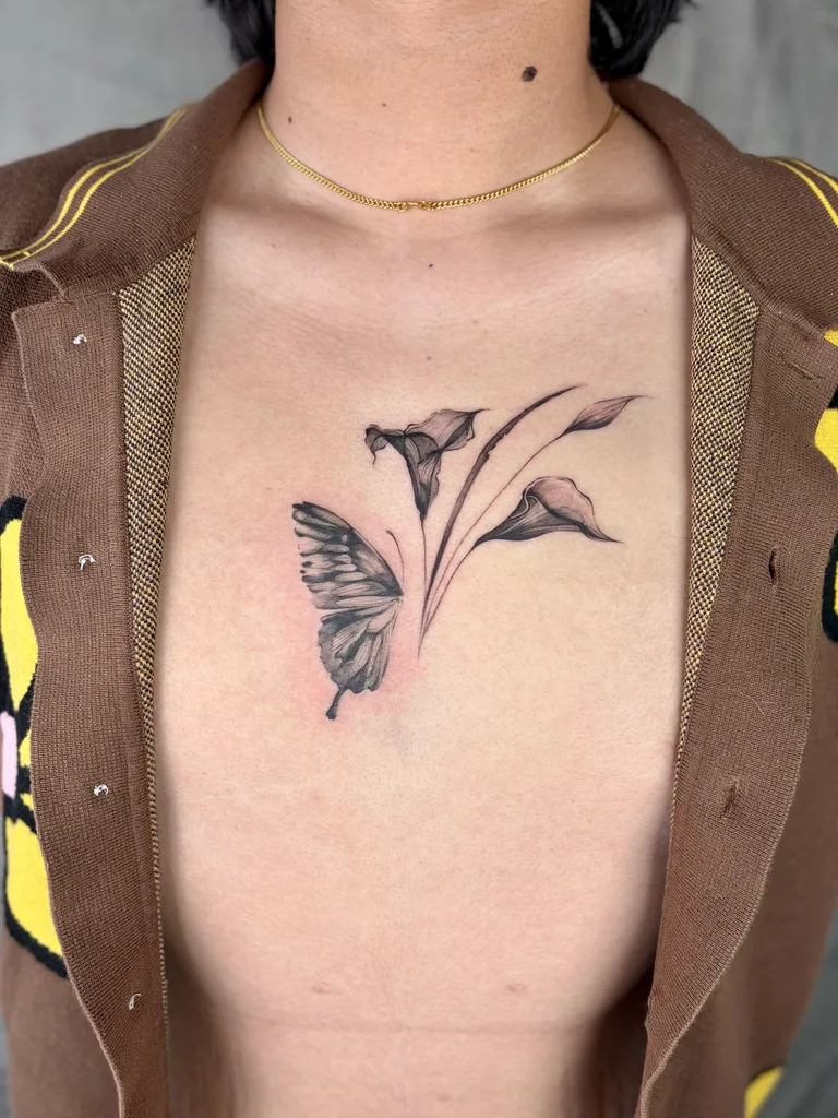 Butterfly lilies tattoo design for women, fine line style, on the sternum, with a butterfly on the left and multiple calla lilies on the right