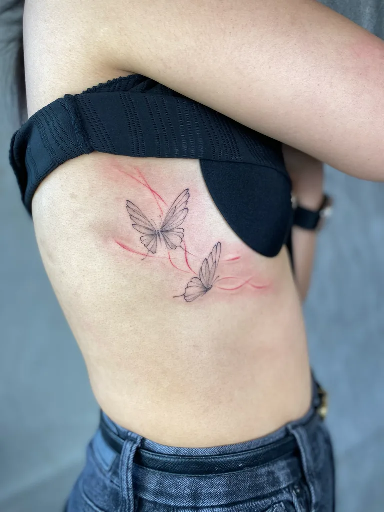 Butterflies tattoo design for women, minimalist style, on the rib, two butterflies with red whip-shading trails along the rib
