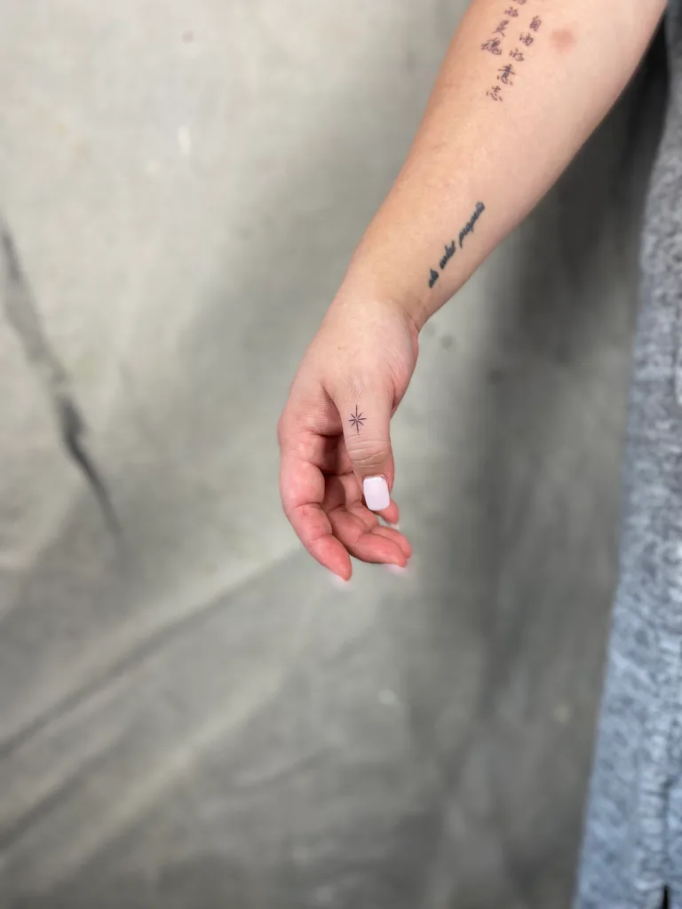 Sparkle star tattoo design for women, minimalist style, on the wrist, tiny sparkle star on the inner wrist beside fine script